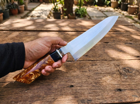 Hand holding a large knife with a wooden handle on a wooden surface